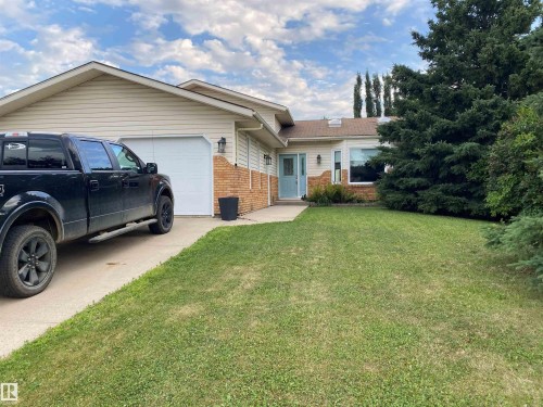The property features a concrete driveway leading to an attached garage, a well-maintained lawn, and mature evergreen trees - 1929 Forest Drive, Cold Lake, AB - Outdoor