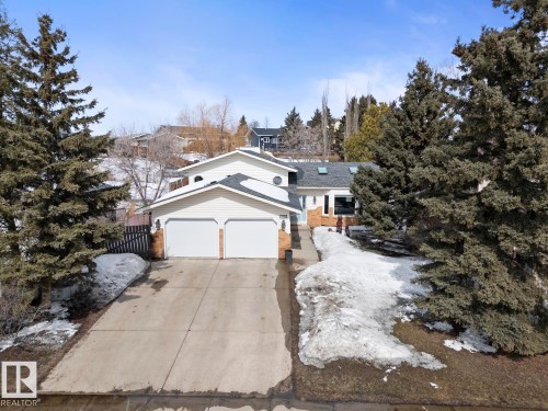 The property features a two-car garage with white doors, a concrete driveway, and a front exterior with light-colored siding and brick accents - 1929 Forest Drive, Cold Lake, AB - Outdoor