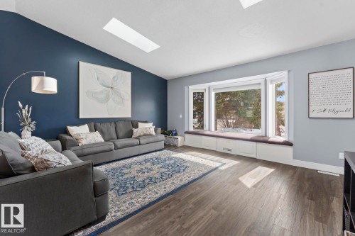 The living area features a vaulted ceiling with a skylight, a bay window with a built-in window seat and storage, and vinyl plank flooring - 1929 Forest Drive, Cold Lake, AB - Indoor Photo Showing Living Room