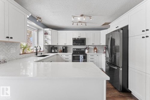 The kitchen features white cabinetry with dark hardware, a white quartz countertop, a herringbone tile backsplash, and dark kitchen appliances - 1929 Forest Drive, Cold Lake, AB - Indoor Photo Showing Kitchen