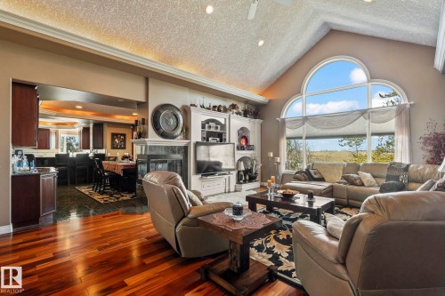 This living space features hardwood floors, a vaulted ceiling, and an arched window offering expansive views - 9610 167 Street Sw, Edmonton, AB - Indoor Photo Showing Living Room