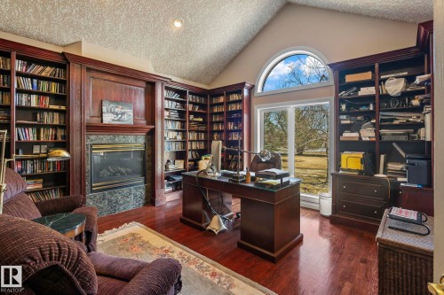 This room features extensive built-in wooden shelving, a fireplace with a stone surround, and hardwood floors - 9610 167 Street Sw, Edmonton, AB - Indoor Photo Showing Office