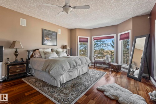 The bedroom features hardwood floors, a ceiling fan, and bay windows with views of trees and open land - 9610 167 Street Sw, Edmonton, AB - Indoor Photo Showing Bedroom