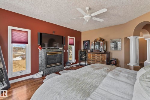 The room features hardwood floors, a fireplace with a stone surround, and windows with horizontal blinds - 9610 167 Street Sw, Edmonton, AB - Indoor Photo Showing Bedroom With Fireplace