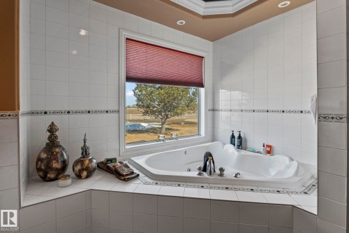 The bathroom features a large corner tub with a window view, surrounded by white tiled walls with a decorative border - 9610 167 Street Sw, Edmonton, AB - Indoor Photo Showing Bathroom