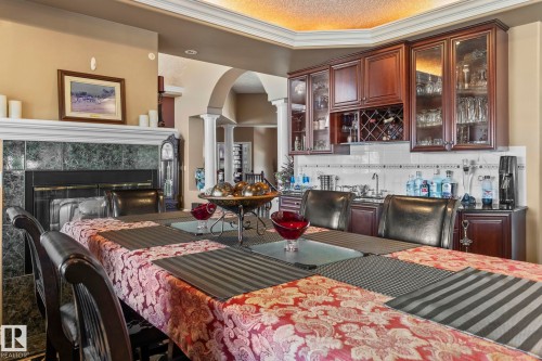 Formal dining space featuring a fireplace with a marble tile surround, built-in cabinetry with glass doors, and a decorative archway - 9610 167 Street Sw, Edmonton, AB - Indoor Photo Showing Dining Room With Fireplace