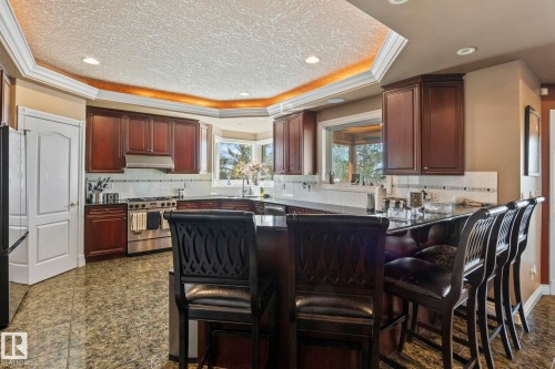 The kitchen features dark wood cabinetry, stainless steel appliances, and a central island with a breakfast bar - 9610 167 Street Sw, Edmonton, AB - Indoor