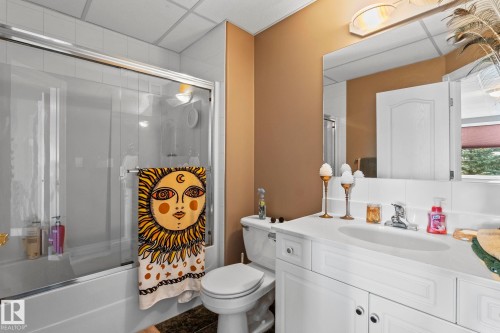 Bathroom featuring a bathtub with a sliding glass door, a toilet, and a vanity with a white countertop and a mirror - 9610 167 Street Sw, Edmonton, AB - Indoor Photo Showing Bathroom