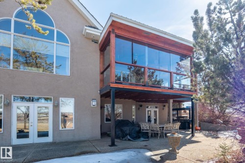 The property features a large two-story window with an arched top, a glass-enclosed balcony with a wooden frame, and a ground-level patio with double white French doors - 9610 167 Street Sw, Edmonton, AB - Outdoor