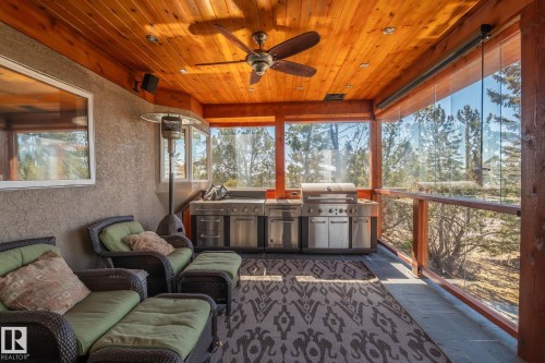 Spacious covered outdoor living area featuring a wood plank ceiling with a ceiling fan, an outdoor kitchen with stainless steel appliances, and glass panel railings - 9610 167 Street Sw, Edmonton, AB - Outdoor With Deck Patio Veranda With Exterior