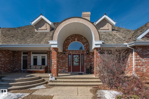 The property features a prominent brick exterior with a large arched entryway and a red front door - 9610 167 Street Sw, Edmonton, AB - Outdoor With Deck Patio Veranda
