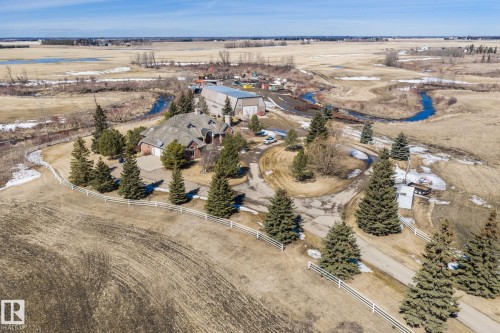 The property features a brick exterior, an attached two-car garage, and a paved driveway, surrounded by mature evergreen trees and a white fence - 9610 167 Street Sw, Edmonton, AB - Outdoor With View