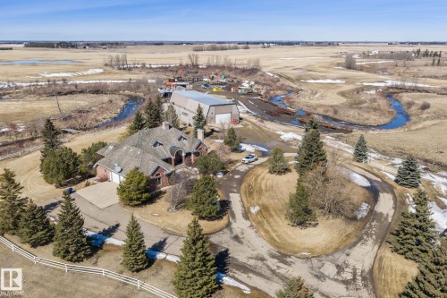 The property features a brick exterior, a driveway, and a paved circular drive, surrounded by mature evergreen trees - 9610 167 Street Sw, Edmonton, AB - Outdoor With View