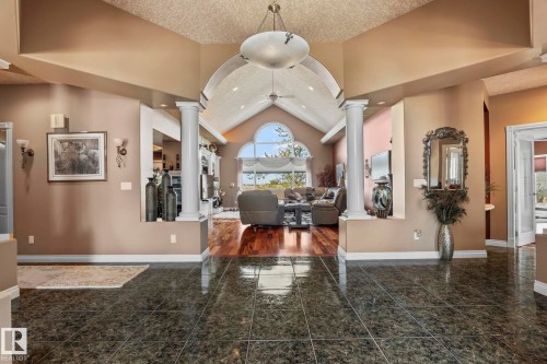 The property features a spacious entry with polished dark tile flooring and columns, leading into a living area with hardwood floors, vaulted ceilings, and large arched windows - 9610 167 Street Sw, Edmonton, AB - Indoor