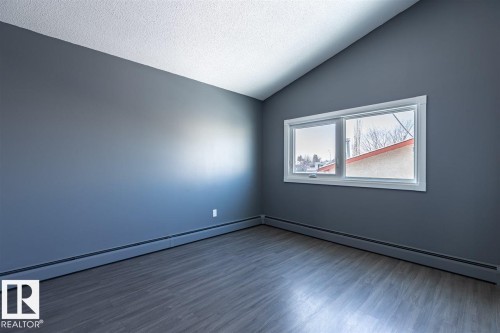 The property features an empty room with a vaulted ceiling, a large window, dark walls, and wood-style flooring - 15204 94 Street, Edmonton, AB - Indoor Photo Showing Other Room