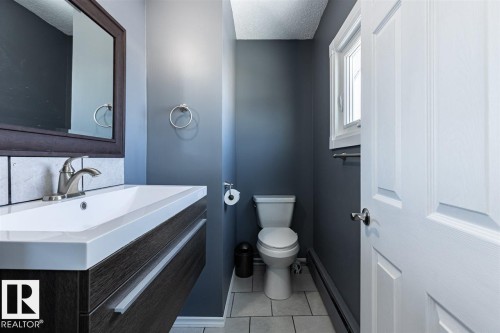 Bathroom featuring a floating vanity with a white rectangular sink, a framed mirror, a toilet, and a window providing natural light - 15204 94 Street, Edmonton, AB - Indoor Photo Showing Bathroom