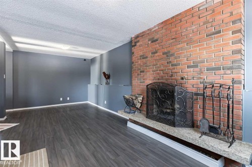 Living area featuring dark gray flooring, a brick accent wall with a fireplace, and a light-colored mantel - 15204 94 Street, Edmonton, AB - Indoor Photo Showing Other Room With Fireplace