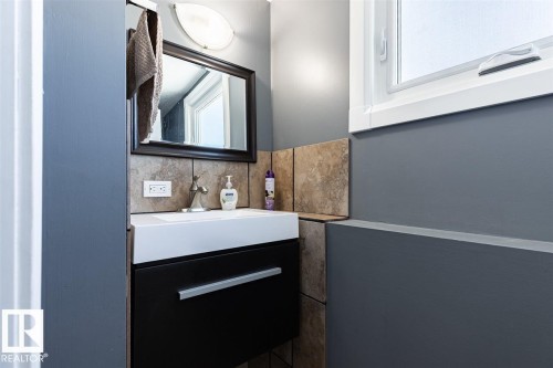 Bathroom featuring a vanity with a white sink, dark cabinetry, and a framed mirror - 15204 94 Street, Edmonton, AB - Indoor