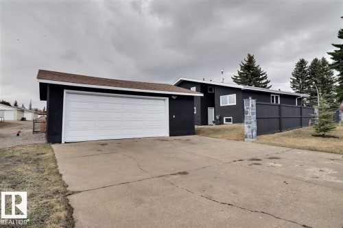 The property features a two-car garage with a white door, a paved driveway, and a fenced yard with mature trees - 15204 94 Street, Edmonton, AB - Outdoor
