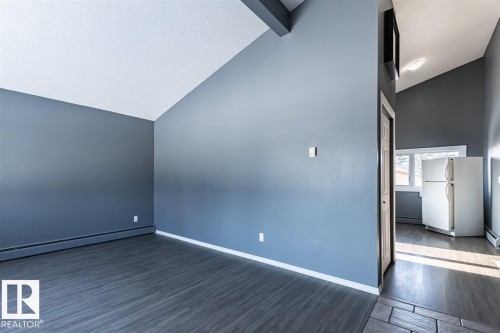The property features vaulted ceilings, dark plank flooring, and a kitchen area with a refrigerator and window - 15204 94 Street, Edmonton, AB - Indoor Photo Showing Other Room