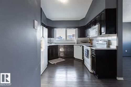 The kitchen features dark cabinetry, white countertops, and white appliances, including a refrigerator, dishwasher, and stove with an overhead microwave - 15204 94 Street, Edmonton, AB - Indoor Photo Showing Kitchen