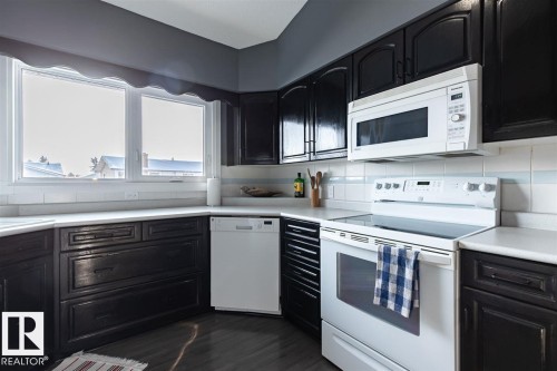 The kitchen features dark wood cabinetry, white countertops, and a white electric range with an overhead microwave - 15204 94 Street, Edmonton, AB - Indoor Photo Showing Kitchen