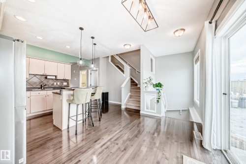 The open concept living area features hardwood floors, a kitchen island with pendant lighting, a stainless steel refrigerator, and a sliding glass door leading to an outdoor space - 105 13825 155 Avenue, Edmonton, AB - Indoor Photo Showing Kitchen With Upgraded Kitchen