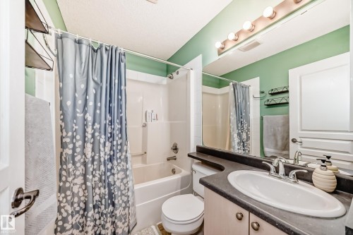 Bathroom featuring a vanity with an integrated sink and a dark countertop, a mirror with overhead lighting, and a bathtub with a shower - 105 13825 155 Avenue, Edmonton, AB - Indoor Photo Showing Bathroom