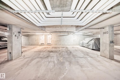Underground parking area featuring concrete floors and walls, with exposed conduit and overhead lighting - 105 13825 155 Avenue, Edmonton, AB - Indoor Photo Showing Garage