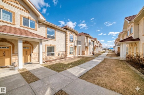 The property features a stucco exterior with stone accents, a red tile roof, and individual front entrances with transom windows - 105 13825 155 Avenue, Edmonton, AB - Outdoor