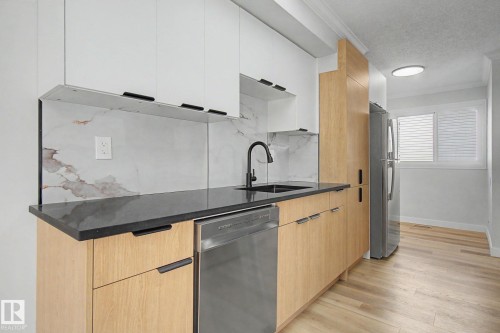 The kitchen features light wood cabinetry, white upper cabinets, a black countertop, and a white backsplash with brown veining - 186 Centennial Crest, Edmonton, AB - Indoor Photo Showing Kitchen