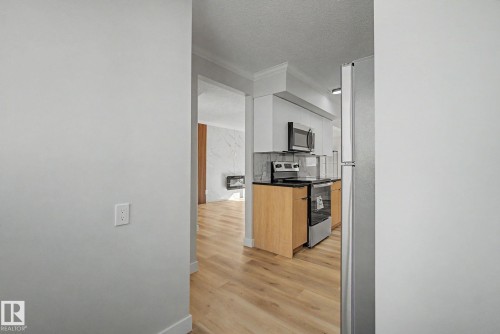 The kitchen features wood cabinetry, stainless steel appliances, and a black countertop, complemented by light-toned flooring - 186 Centennial Crest, Edmonton, AB - Indoor Photo Showing Kitchen