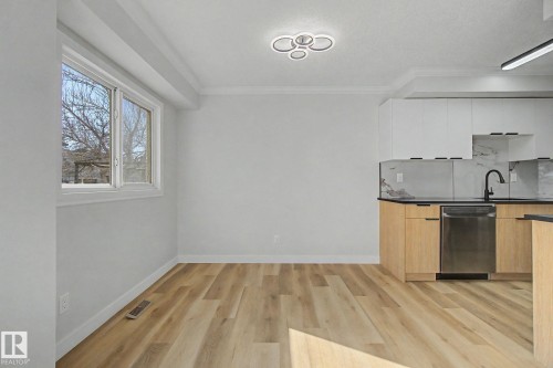 The property features light-toned flooring, a bright window, and a kitchen area with white upper cabinetry, light wood lower cabinetry, and a stainless steel dishwasher - 186 Centennial Crest, Edmonton, AB - Indoor