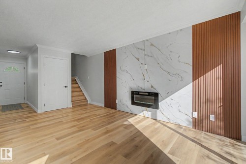 The living area features light-toned hardwood flooring and a stylish accent wall with a built-in fireplace - 186 Centennial Crest, Edmonton, AB - Indoor Photo Showing Other Room With Fireplace