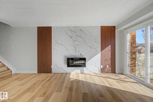 Living area featuring light wood flooring, a fireplace with a white marble-patterned surround, and a sliding glass door providing natural light - 186 Centennial Crest, Edmonton, AB - Indoor With Fireplace