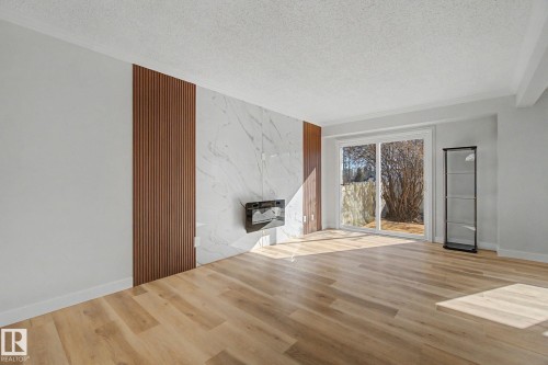 Spacious living area featuring light-colored flooring, a decorative wall panel with a white marble-effect finish, and a modern wall-mounted fireplace - 186 Centennial Crest, Edmonton, AB - Indoor Photo Showing Living Room With Fireplace
