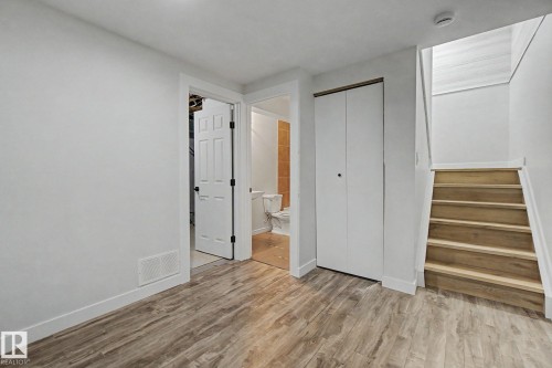 The room features wood-look flooring and white walls, with a white door and closet, and a wooden staircase - 186 Centennial Crest, Edmonton, AB - Indoor Photo Showing Other Room