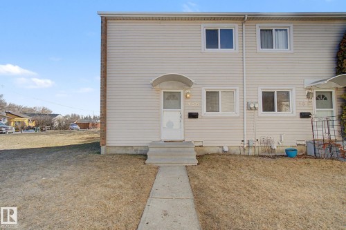 Exterior view of the property featuring light-colored siding, white-trimmed windows, a front door with an awning, and concrete steps leading to a paved walkway - 186 Centennial Crest, Edmonton, AB - Outdoor With Exterior