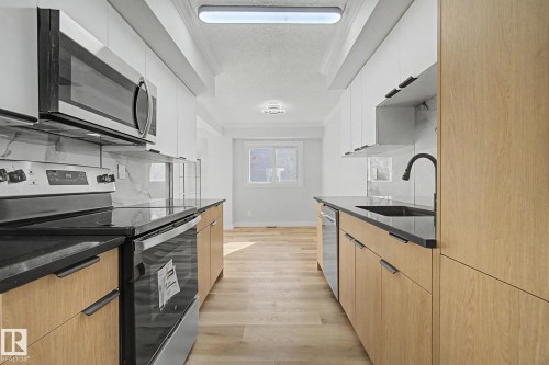 The kitchen features light wood cabinetry, dark countertops, a black sink with a black faucet, and stainless steel appliances including a microwave, oven, and dishwasher - 186 Centennial Crest, Edmonton, AB - Indoor Photo Showing Kitchen
