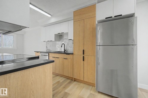 Modern kitchen featuring light wood cabinetry, white upper cabinets, a stainless steel refrigerator, and dark countertops - 186 Centennial Crest, Edmonton, AB - Indoor Photo Showing Kitchen