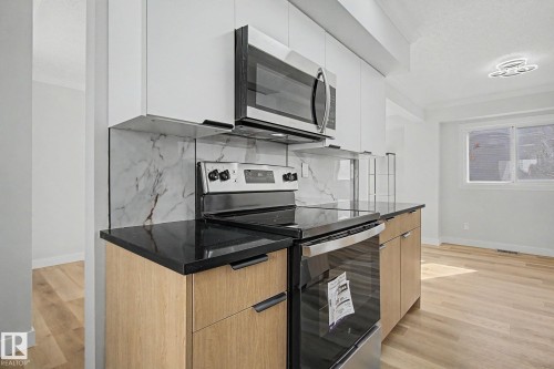 The kitchen features stainless steel appliances, including a microwave and range, set against a marble-patterned backsplash - 186 Centennial Crest, Edmonton, AB - Indoor Photo Showing Kitchen