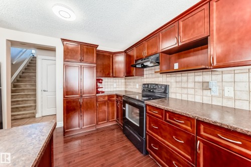 The kitchen features rich wood cabinetry, a tiled backsplash, and dark countertops - 11415 167A Avenue, Edmonton, AB - Indoor Photo Showing Kitchen