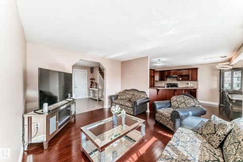 The open concept living area features hardwood flooring, a clear view of the kitchen with dark wood cabinetry and a breakfast bar, and a distinct dining area with a modern chandelier - 11415 167A Avenue, Edmonton, AB - Indoor Photo Showing Living Room