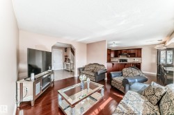 The open concept living area features hardwood flooring, a clear view of the kitchen with dark wood cabinetry and a breakfast bar, and a distinct dining area with a modern chandelier - 