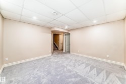 Spacious room with light-colored walls and plush grey carpeting, featuring recessed lighting and a drop ceiling - 