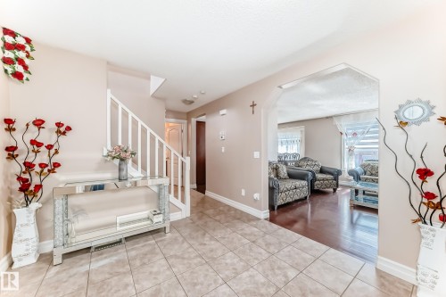 The foyer features tiled flooring and a staircase with white railings, leading to an arched entryway revealing a living area with hardwood floors - 11415 167A Avenue, Edmonton, AB - Indoor Photo Showing Other Room