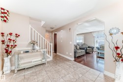 The foyer features tiled flooring and a staircase with white railings, leading to an arched entryway revealing a living area with hardwood floors - 