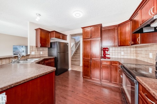 The kitchen features extensive dark wood cabinetry, a double basin stainless steel sink, and a black range with an overhead vent - 11415 167A Avenue, Edmonton, AB - Indoor Photo Showing Kitchen With Double Sink