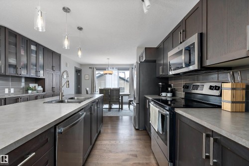 Modern kitchen featuring dark wood cabinetry, stainless steel appliances, light-colored countertops, and hardwood flooring - 7776 Eifert Crescent Nw, Edmonton, AB - Indoor Photo Showing Kitchen With Double Sink With Upgraded Kitchen