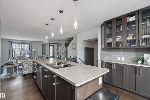 The kitchen features a large island with a double sink, pendant lighting, and dark wood cabinetry with glass fronts - 7776 Eifert Crescent Nw, Edmonton, AB - Indoor Photo Showing Kitchen With Double Sink With Upgraded Kitchen